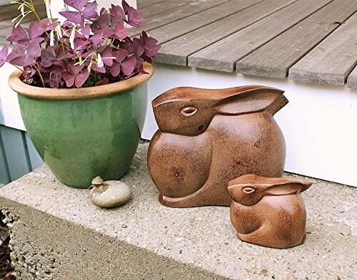 Ceramic bunny sculptures next to a green potted plant on a porch.