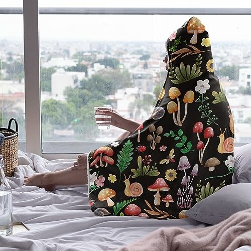 Person in a hooded blanket with nature design sitting by a window.