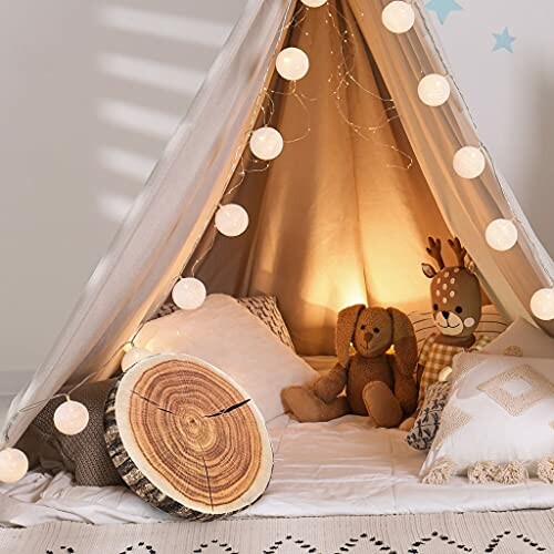 Cozy kids' play tent with string lights, pillows, and stuffed toys.