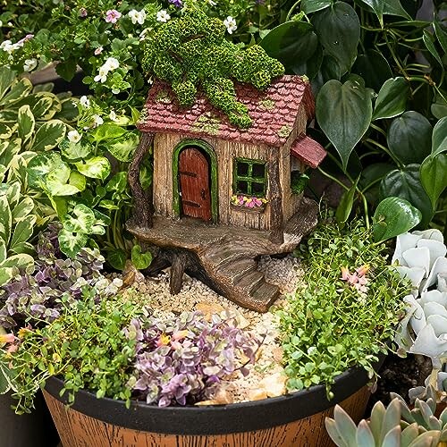 Miniature fairy house surrounded by lush plants and flowers in a pot.