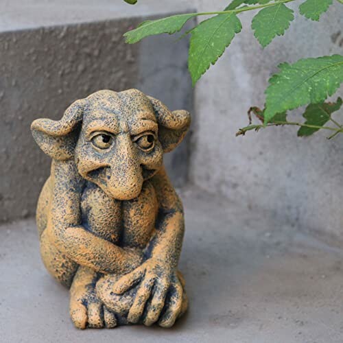 A small stone goblin statue on steps with plant leaves nearby.