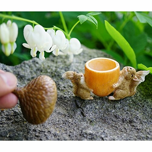 Two mice figurines with a cup and a hand holding an acorn on a rock.